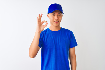 Chinese deliveryman wearing blue t-shirt and cap standing over isolated white background smiling positive doing ok sign with hand and fingers. Successful expression.