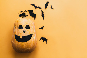 Halloween flat lay. Pumpkin with face and black bats paper decorations on yellow background, copy...