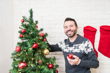 Portrait Of Male Decorating Tree During Christmastime At Home