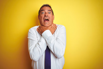 Obraz premium Handsome middle age businessman standing over isolated yellow background shouting and suffocate because painful strangle. Health problem. Asphyxiate and suicide concept.