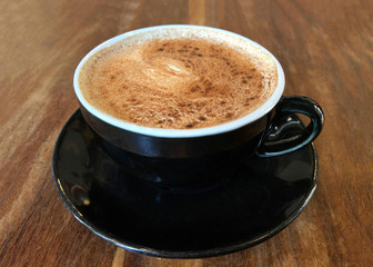 Chai Latte in a black cup on saucer served on dark wood stressed cafe table. Popular tea beverage. Side view.
