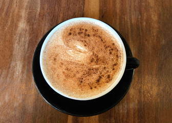 Flat lay top view of one Chai Latte in a black cup on saucer served on dark wood stressed cafe table. Popular tea beverage.