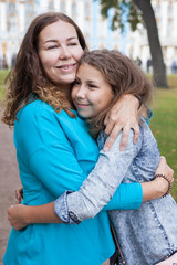 Fototapeta premium Happy mother embracing her teenage daughter, Caucasian long hair females, standing outdoor
