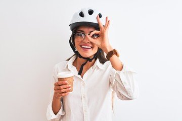 Beautiful businesswoman wearing bike helmet drinking coffee over isolated white background with happy face smiling doing ok sign with hand on eye looking through fingers