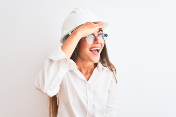 Young beautiful architect woman wearing helmet and glasses over isolated white background very happy and smiling looking far away with hand over head. Searching concept.