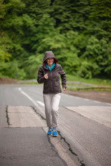 One mature woman, running outdoors on a asphalt road, in a nature.