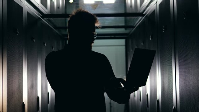 Silhouette of a male technician is working in a dark server room.
