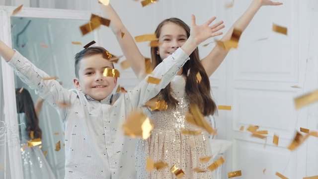 Portrait of happy children throwing golden confetti into camera.