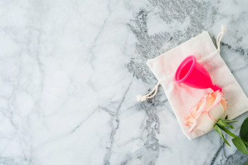 Pink menstrual cup with cotton bag on marble table. Zero waste product for body care