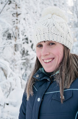 Happy and smiling young woman portrait dressed with white winter hat, snowy trees as background