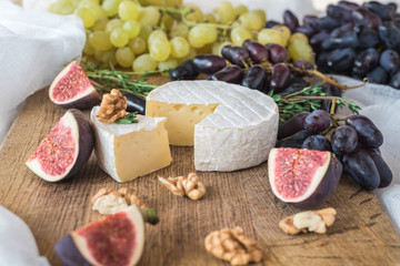 View of a wooden board with the head of white Camembert cheese and cut figs, nuts 