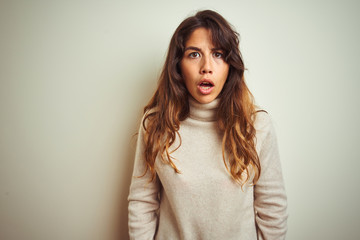 Fototapeta premium Young beautiful woman wearing winter sweater standing over white isolated background afraid and shocked with surprise and amazed expression, fear and excited face.