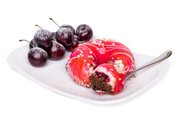 Elegant striped sponge cake with a shiny glaze, coconut flakes and sugar pearls in the shape of a doughnut. Piece on a fork, sweet cherries with powdered sugar