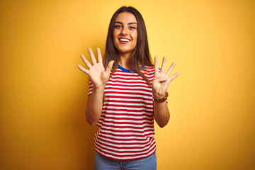Young beautiful woman wearing striped t-shirt standing over isolated yellow background showing and...