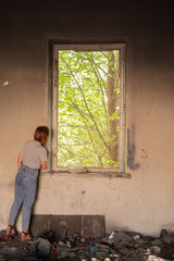 Fototapeta premium girl in a dirty room looks out of the window at green trees. Environmental pollution. Changing of the climate.