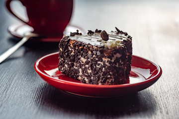 A delicious heart-shaped cake sprinkled with pieces of chocolate lies on a red plate. Photographed close-up on a wooden background.