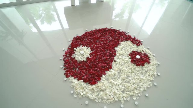 Yin yang simbol of red and white rose petals on the white floor and a woman's legs in a long white dress
