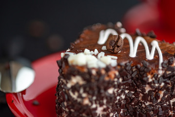 A delicious heart-shaped cake sprinkled with pieces of chocolate lies on a red plate. Photographed close-up on a wooden background.