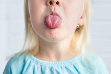 child with blond hair shows tongue closeup. © Maria