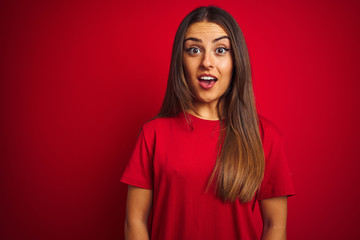 Young beautiful woman wearing t-shirt standing over isolated red background afraid and shocked with surprise expression, fear and excited face.