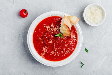 Tomato basil soup with parmesan cheese and bread toasts on gray stone background