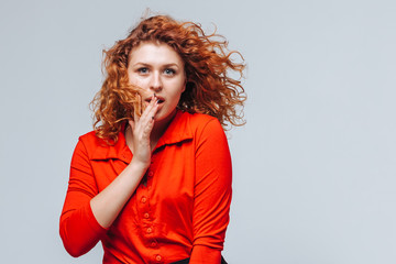 Redhead girl covered her mouth with a finger. the concept of the secret