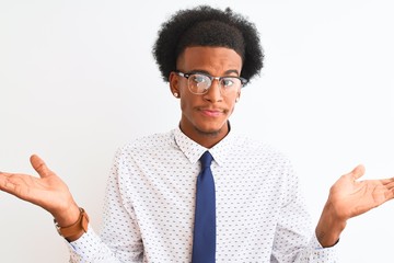 Young african american businessman wearing tie and glasses over isolated white background clueless...