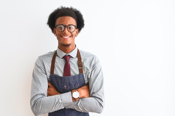 Young african american shopkeeper man wearing apron glasses over isolated white background happy face smiling with crossed arms looking at the camera. Positive person. - obrazy, fototapety, plakaty
