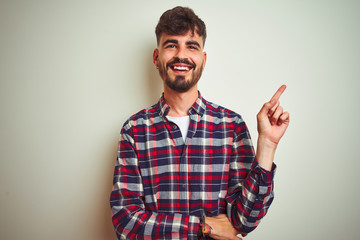 Fototapeta premium Young man wearing casual shirt standing over isolated white background with a big smile on face, pointing with hand and finger to the side looking at the camera.