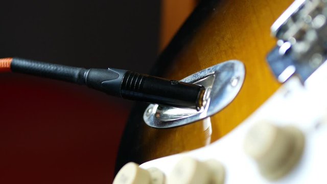 Guitarist plugs instrument cable jack into an electric guitar