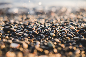 Small stones by the sea with bokeh effect. Blurred decorative background, place for text. Summer wallpaper, sunny sunset light.