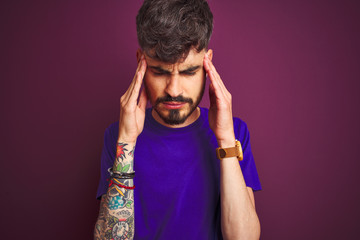 Young man with tattoo wearing t-shirt standing over isolated purple background with hand on head for pain in head because stress. Suffering migraine.