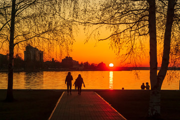 Hot summer sunset on city promenade of lake and silhouettes of people