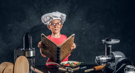 Small kid have a great idea about cooking - he is reading recipe book.