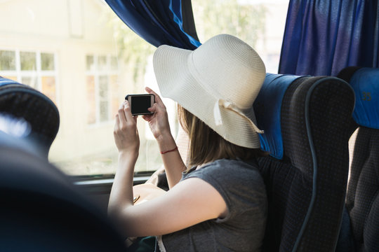 Young woman tourist in hat sits on a bus and takes a selfie on the phone.