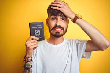 Young man with tattoo wearing Italy Italian passport over isolated yellow background stressed with hand on head, shocked with shame and surprise face, angry and frustrated. Fear and upset for mistake.