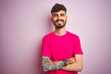 Young man with tattoo wearing t-shirt standing over isolated pink background happy face smiling...