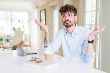 Fototapeta premium Young business man working clueless and confused expression with arms and hands raised. Doubt concept.
