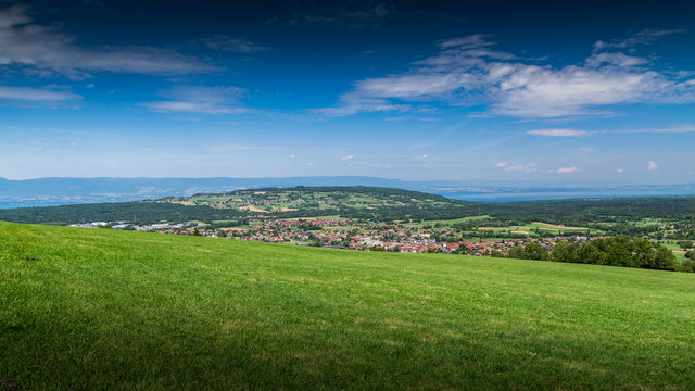  City landscape in the mountains, hills, fields, forests, green meadows, lakes in the distance and blue sky with clouds,focus area in the city.Town Bons-en-Chablais, Haute-Savoie in France.
