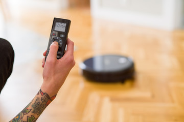 Close up of man hands controling automatic vacuum cleaner using electronic control of the mopping robot