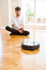Young man using automatic vacuum cleaner to clean the floor, controling machine housework robot