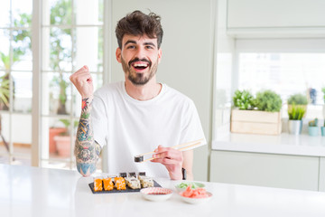 Young man eating asian sushi from home delivery screaming proud and celebrating victory and success very excited, cheering emotion