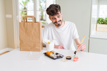 Young man eating sushi asian food and noodles using choopsticks from take away delivery