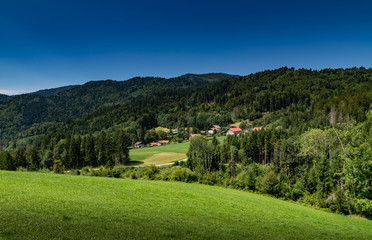 Fototapeta na wymiar Nature and landscape concept: mountain hill landscape overgrown with forests and country houses with blue sky,focus area on country houses.Haute-Savoie in France.