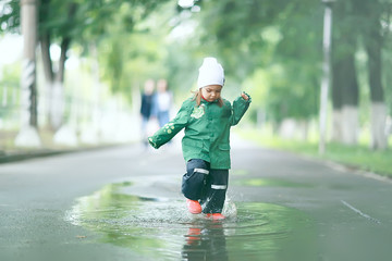 cheerful little girl walks and jumps in puddles in the rain