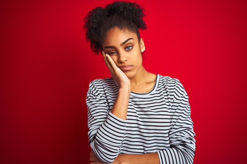 Fototapeta na wymiar African american woman wearing navy striped t-shirt standing over isolated red background thinking looking tired and bored with depression problems with crossed arms.