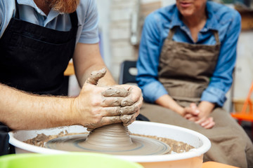 Senior woman spinning clay on a wheel with teacher at pottery class