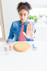 Young african american woman eating homemade cheese pizza with open hand doing stop sign with serious and confident expression, defense gesture