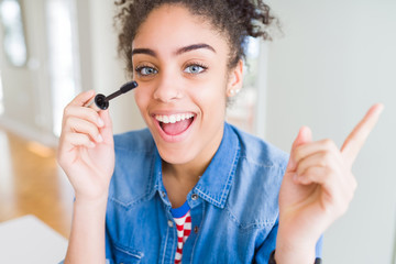 Young african american girl applying eyelashes mascara very happy pointing with hand and finger to the side