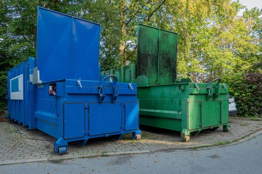 in the courtyard of a hospital there are two garbage compactors next to each other, one for garbage, the other for paper and cardboard